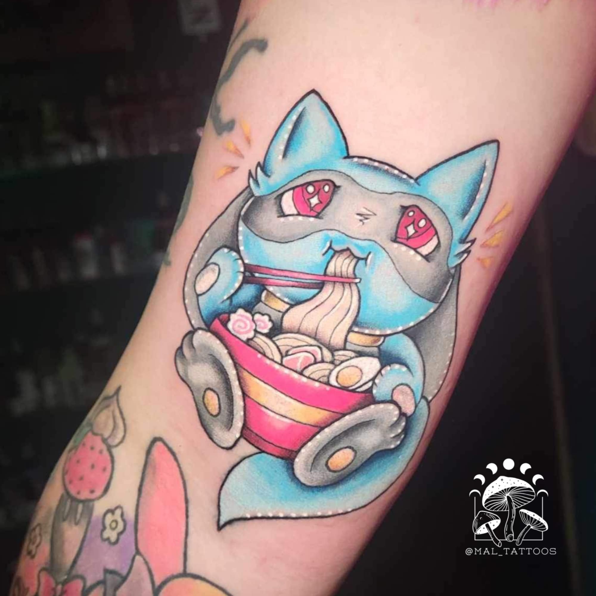 Colorful tattoo of a cat-like creature eating ramen on a person's arm. Pokemon riolu artist rendition