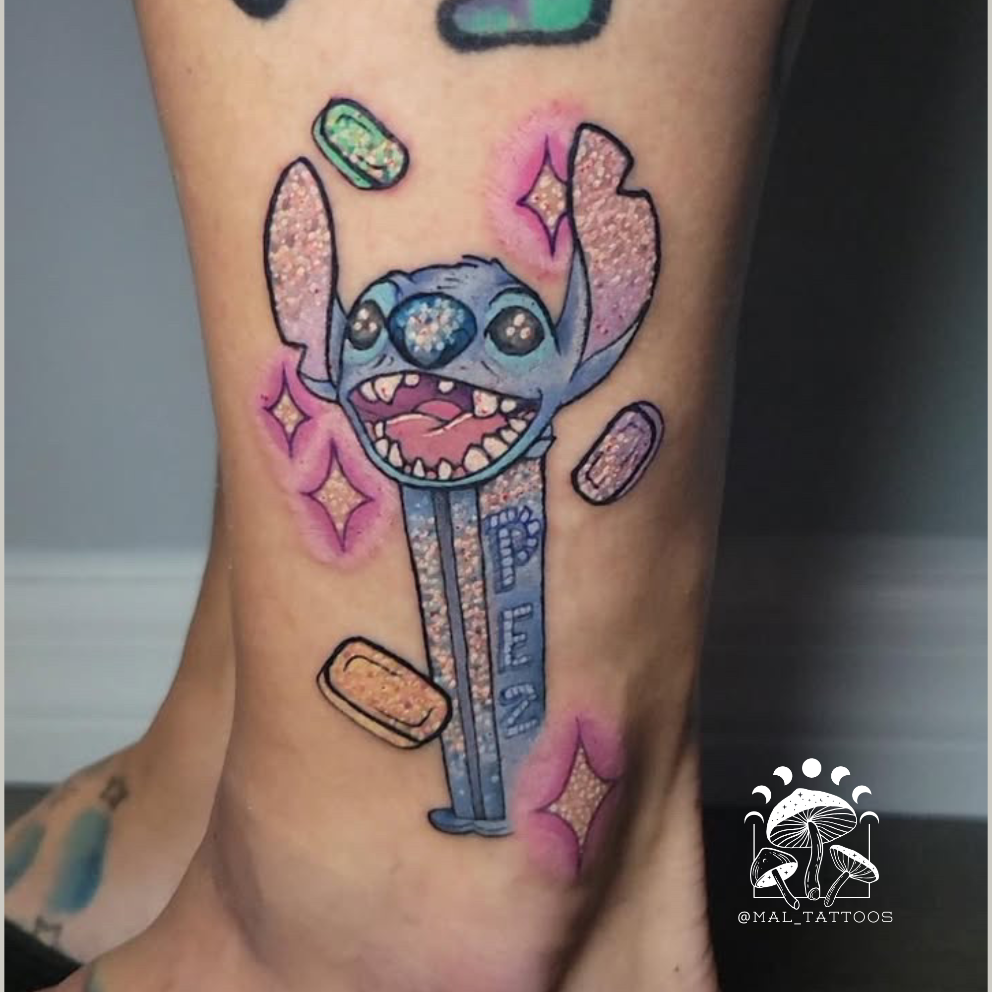Colorful tattoo of a Stitch cartoon character on a person's arm with a blurred background. Lilo & Stitch movie themed tattoo with floatin candy and stars