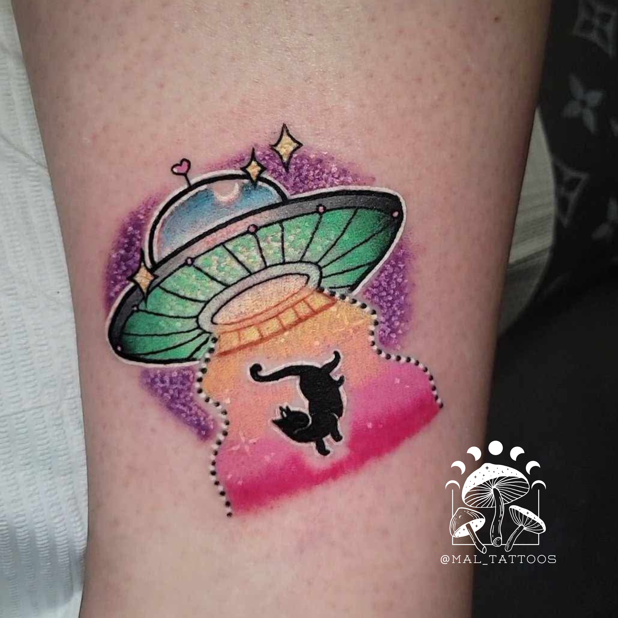 Colorful tattoo of a UFO and cat on a person's leg with 'MAL Tattoos' logo.